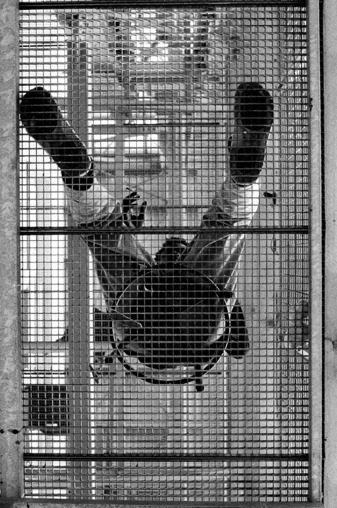 Contre-plongée à travers une résille métallique sur une personne assise sur une chaise, jambes levées, École des Beaux-Arts de Nantes, argentique noir et blanc