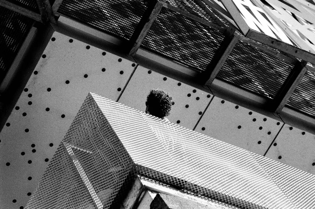 Contre-plongée sur une façade en résille métallique avec une tête qui dépasse, Île de Nantes, Ilford HP5