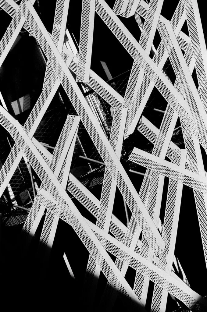 Enchevêtrement de lattes métalliques perforées en diagonales croisées, gros plan, argentique noir et blanc