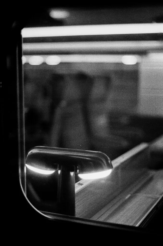 Lampe TGV d'Ionna Vautrin contre la vitre d'un wagon, lumières du quai en arrière-plan, Ilford HP5