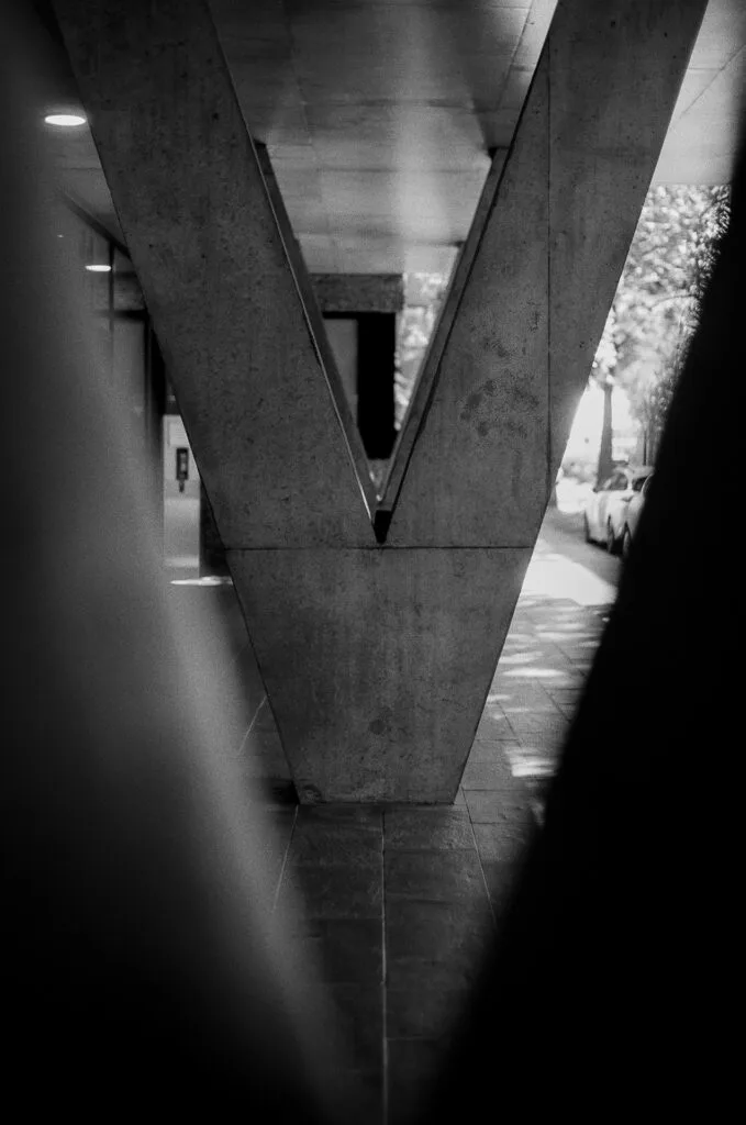 Passage symétrique sous un bâtiment sur pilotis, structure en béton en V, Île de Nantes, argentique noir et blanc