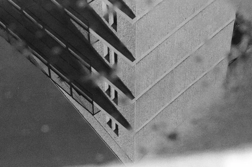 Reflet dans une flaque d'un angle de bâtiment en béton et de ses loggias, argentique noir et blanc