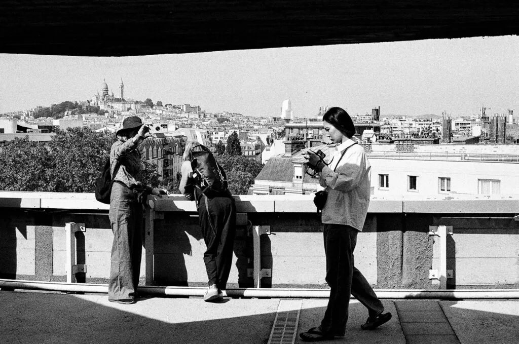 Visiteurs photographiant Paris sous l'avancée de béton du toit-terrasse, Sacré-Cœur au fond