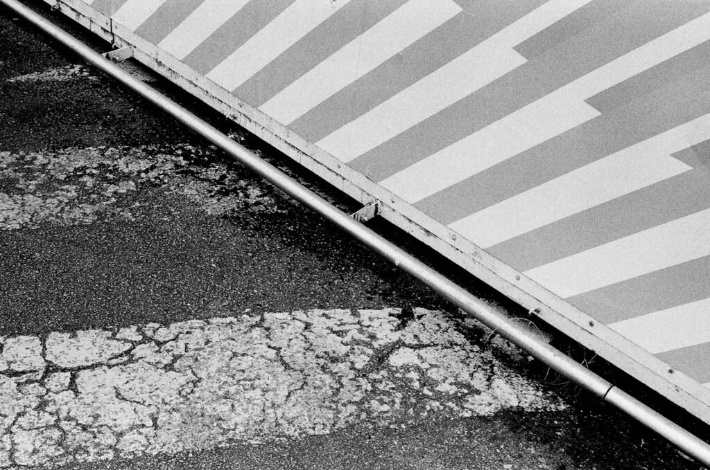 Barrière de chantier rayée et barre métallique traversant l'image en diagonale au-dessus d'un asphalte craquelé