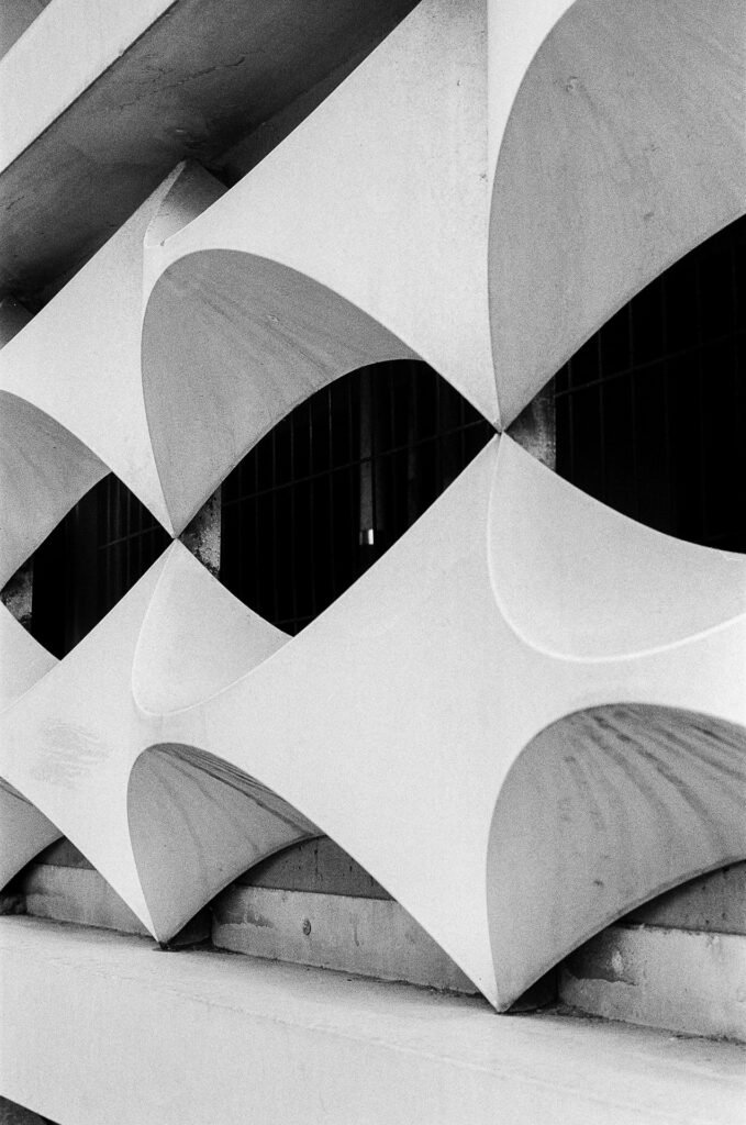 Gros plan sur des claustras en béton aux formes courbes, jeu d’ombres et de lumière en noir et blanc