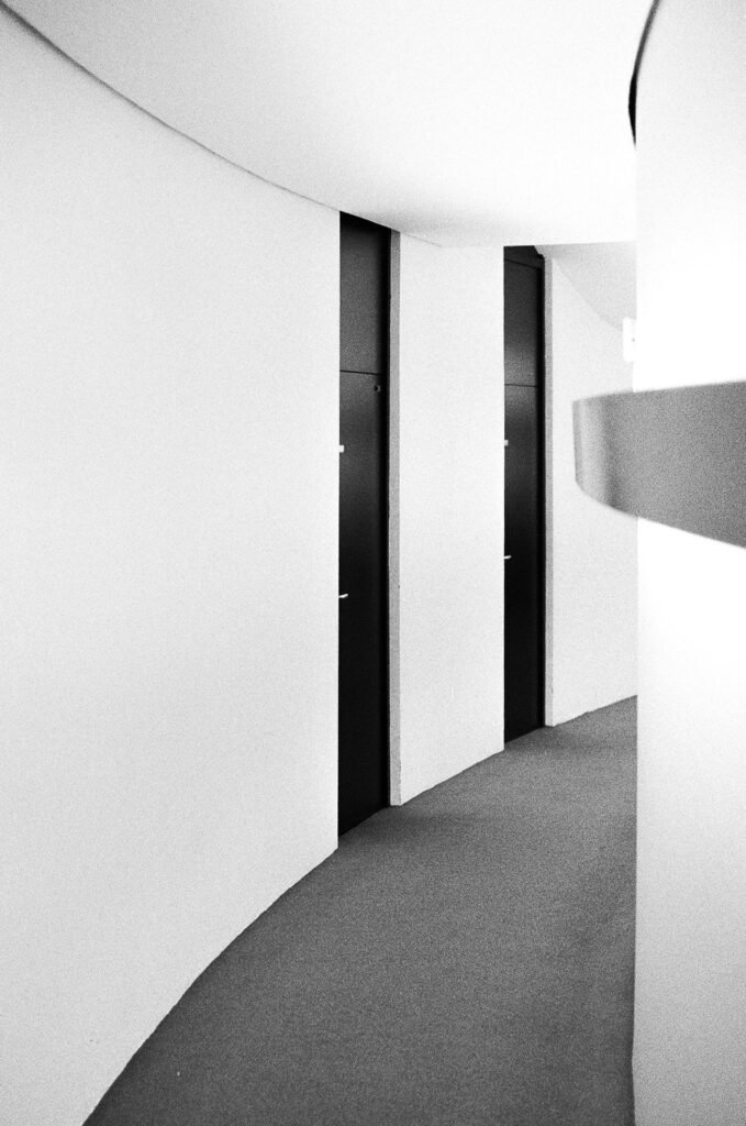 Couloir courbe aux murs blancs et portes noires, siège du PCF, Espace Niemeyer, Paris, argentique noir et blanc