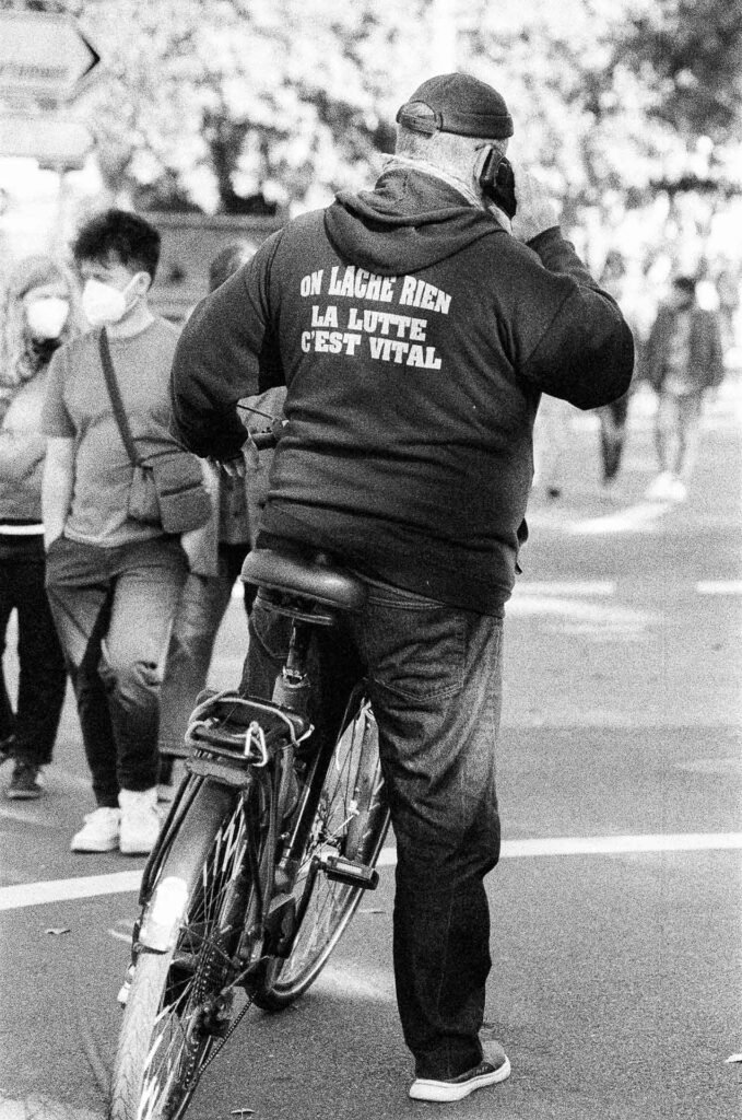 Cycliste vu de dos portant un sweat « On lâche rien, la lutte c'est vital » au bord du cortège à Nantes