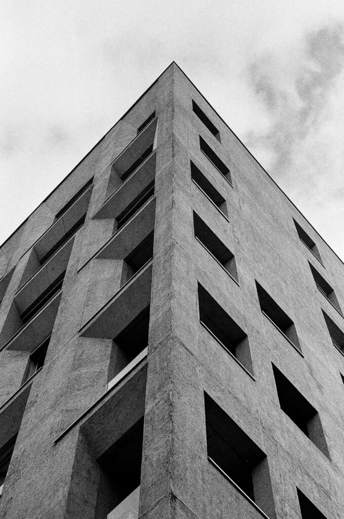 Angle d'un immeuble en béton photographié en contre-plongée sous un ciel nuageux, avec ses fenêtres en retrait