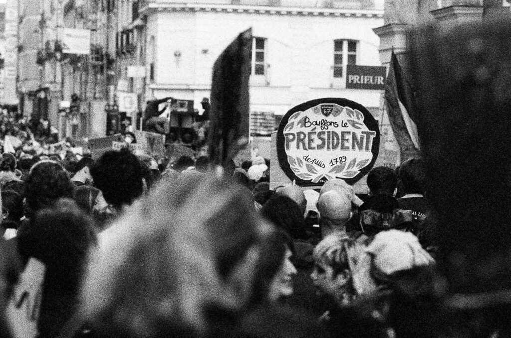 Pancarte ronde imitant une étiquette de camembert au-dessus de la foule dans une rue du centre de Nantes