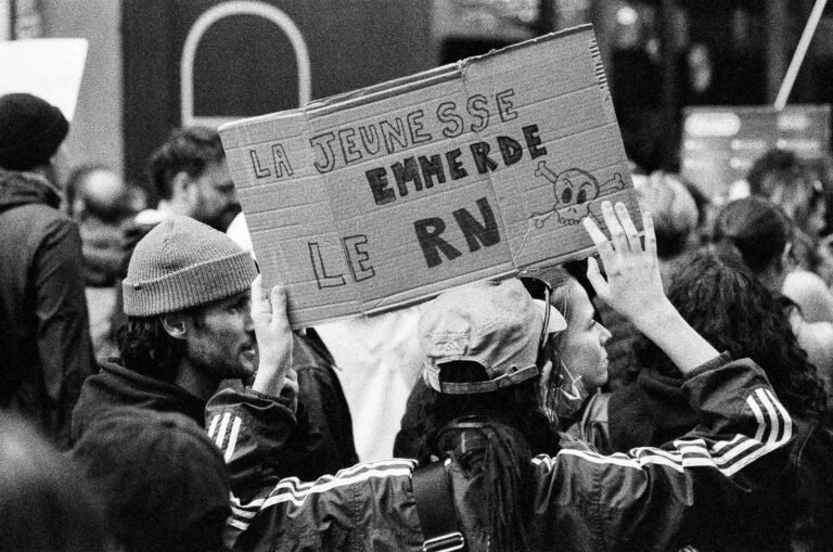 Pancarte « La jeunesse emmerde le RN » avec une tête de mort dessinée, tenue au-dessus des têtes par deux jeunes manifestants