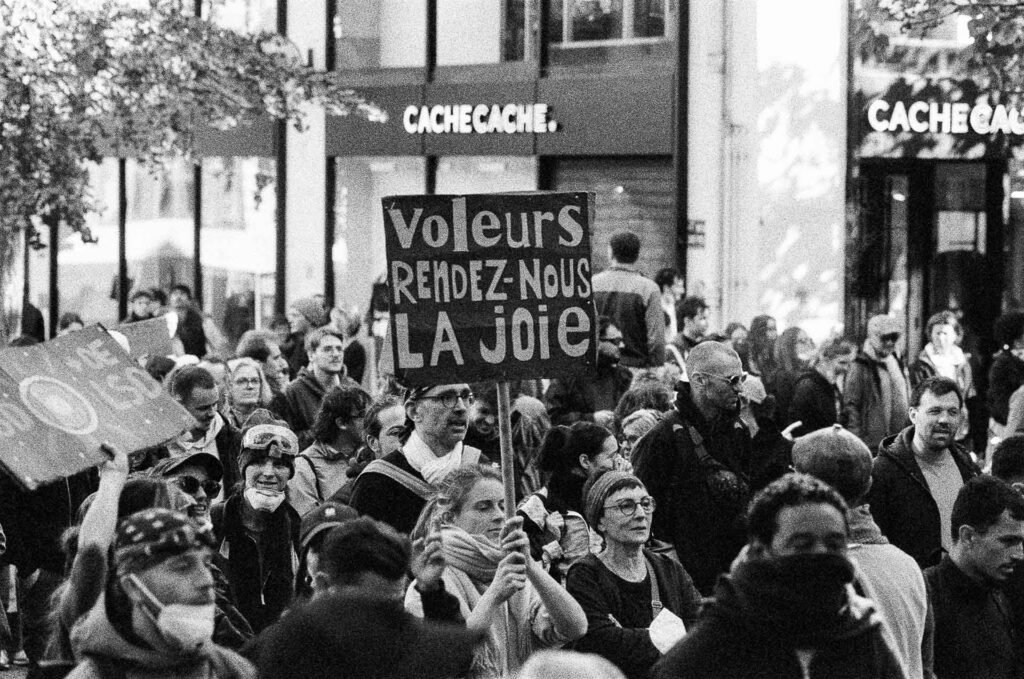 Pancarte « Voleurs rendez-nous la joie » brandie au-dessus de la foule dans une rue commerçante du centre de Nantes