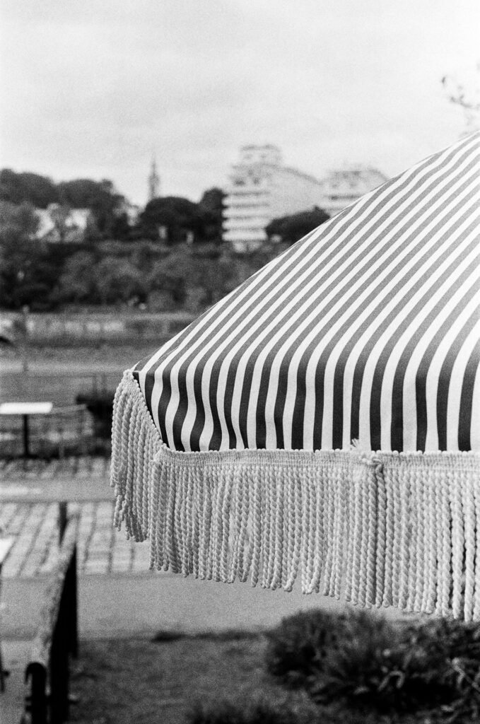 Parasol à rayures et à franges net à f/2, devant une vue floue de Nantes avec arbres et immeubles