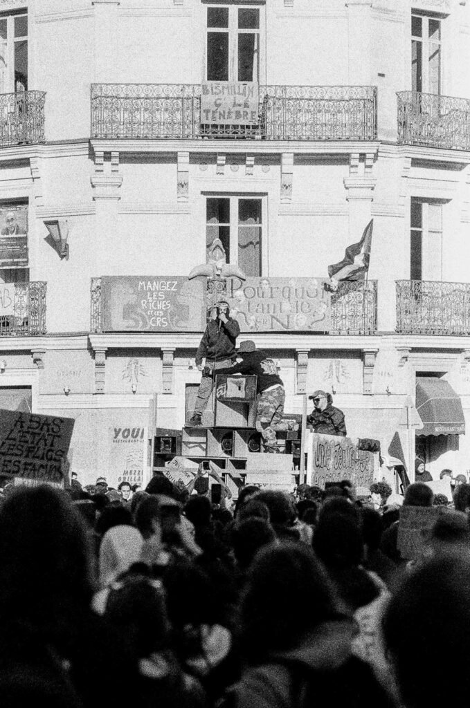 Sound system installé sur un camion devant un immeuble à balcons couvert de banderoles, foule de manifestants au premier plan, Nantes