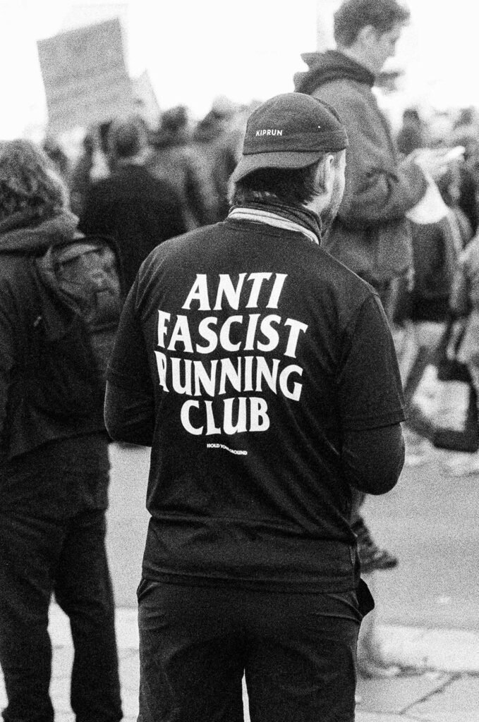 Homme vu de dos portant un t-shirt noir « Anti Fascist Running Club » et une casquette de course, dans le cortège à Nantes