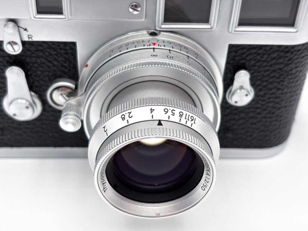 Gros plan sur l’objectif Thypoch Eureka 50mm f/2 monté sur un Leica M3, avec sa bague d’ouverture graduée de f/2 à f/16, son échelle de profondeur de champ et son levier de verrouillage de la mise au point