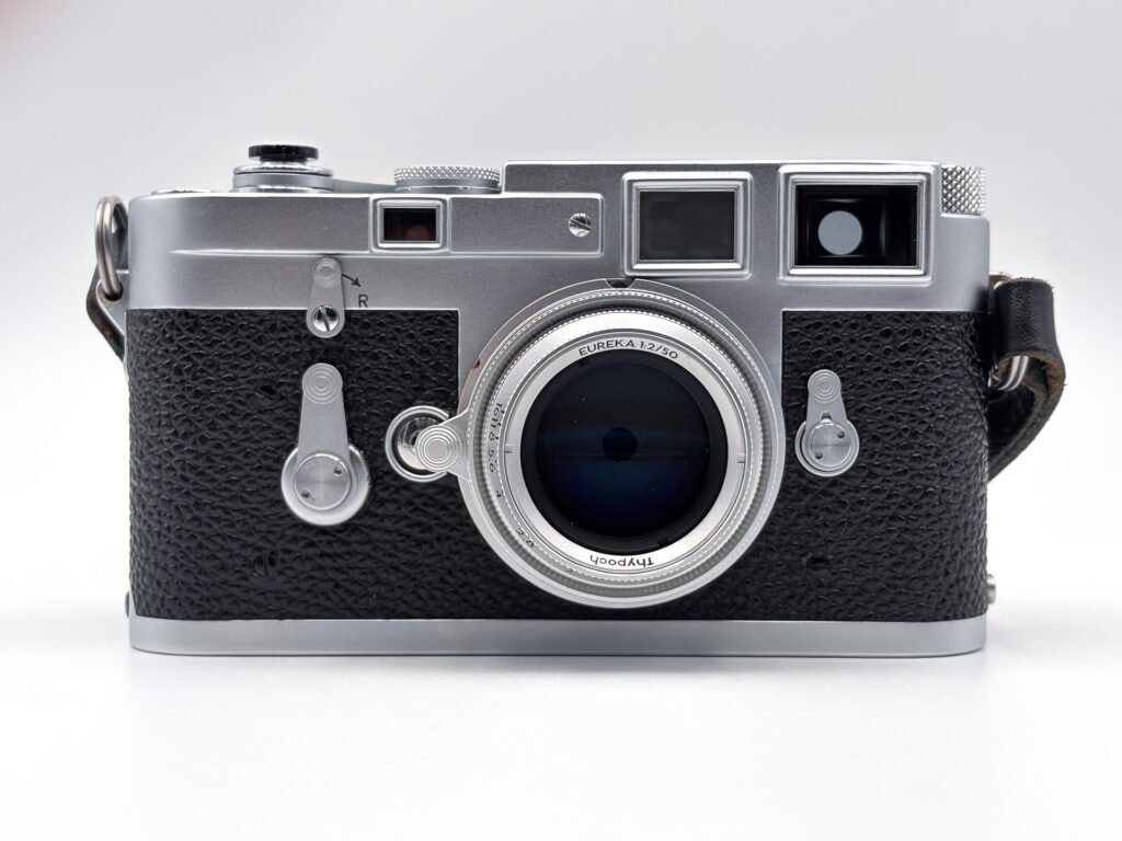 Leica M3 chromé vu de face, équipé de l’objectif Thypoch Eureka 50mm f/2 en aluminium en position rentrée, avec les reflets bleutés du traitement de la lentille frontale